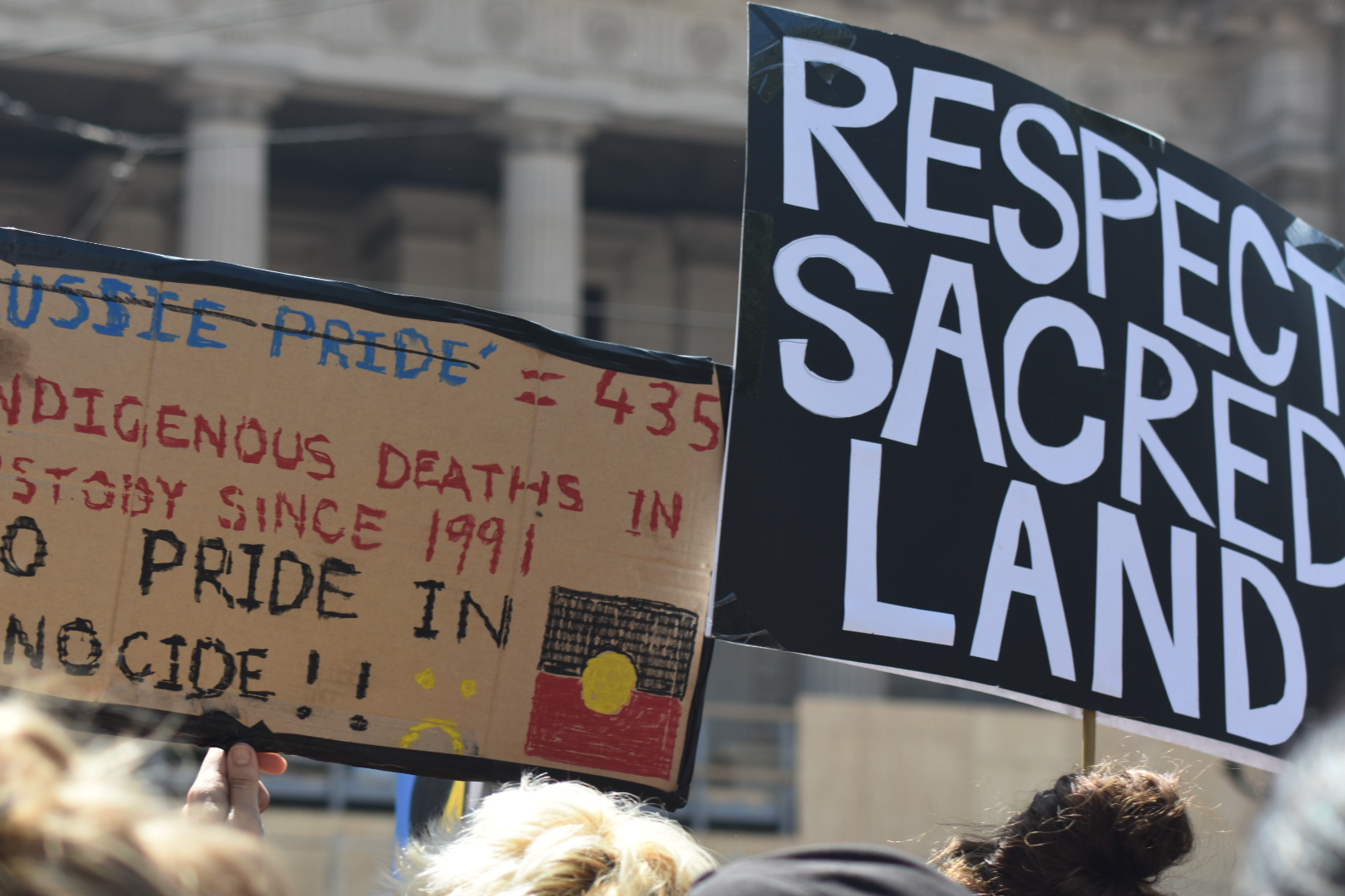 Invasion Day 2020 signs: 'Respect Sacred Land' & 'No Pride in Genocide'
