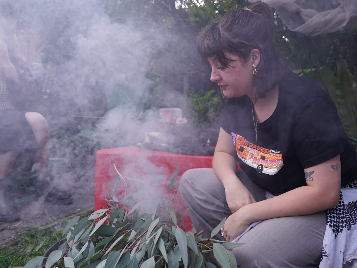 Brittney Henderson squatting next to the sacred flame at a Smoking Ceremony, gazing pensivley into the flame.