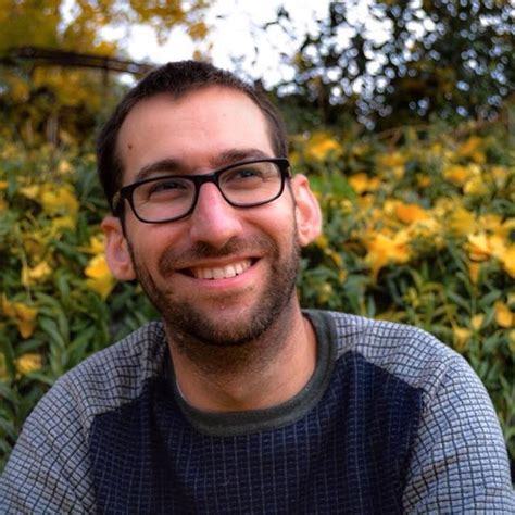 portrait profile pic of Noah Riseman black rimmed glasses beard grey and black top