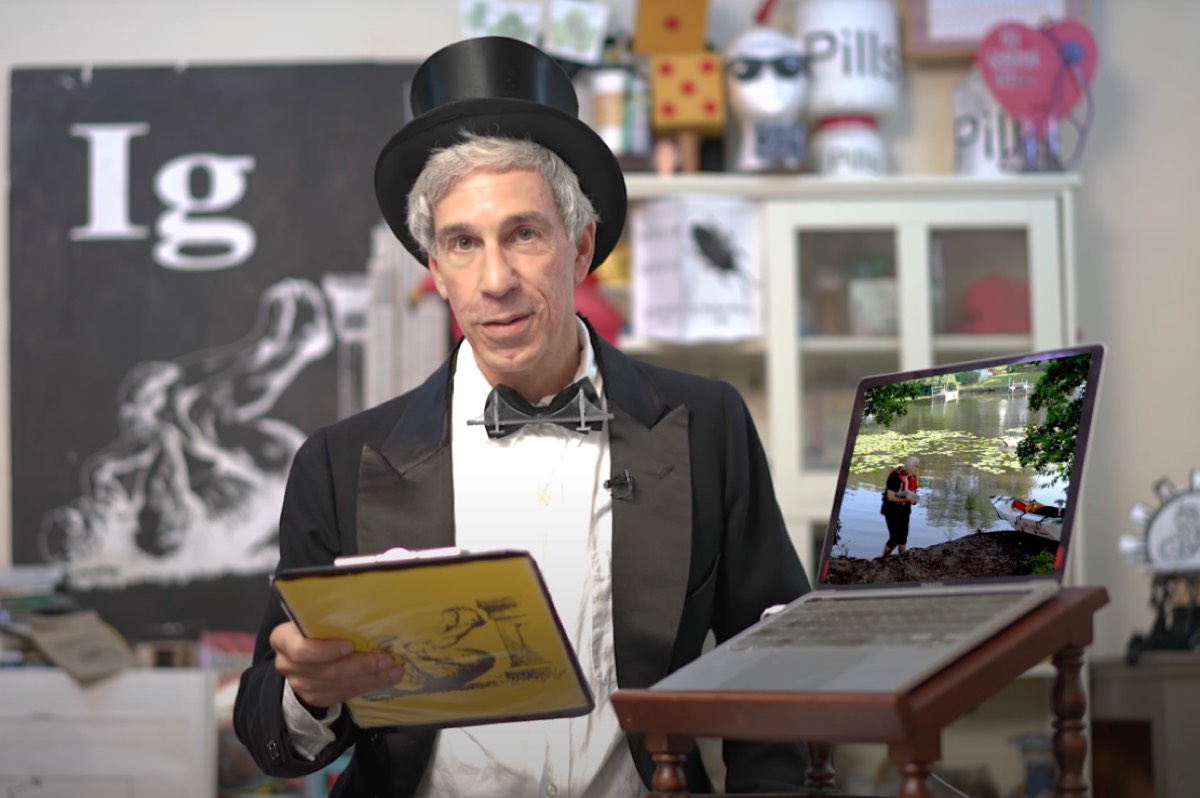Ig Nobel prize emcee Marc Abraham at the lecturn with a top hat and clipboard