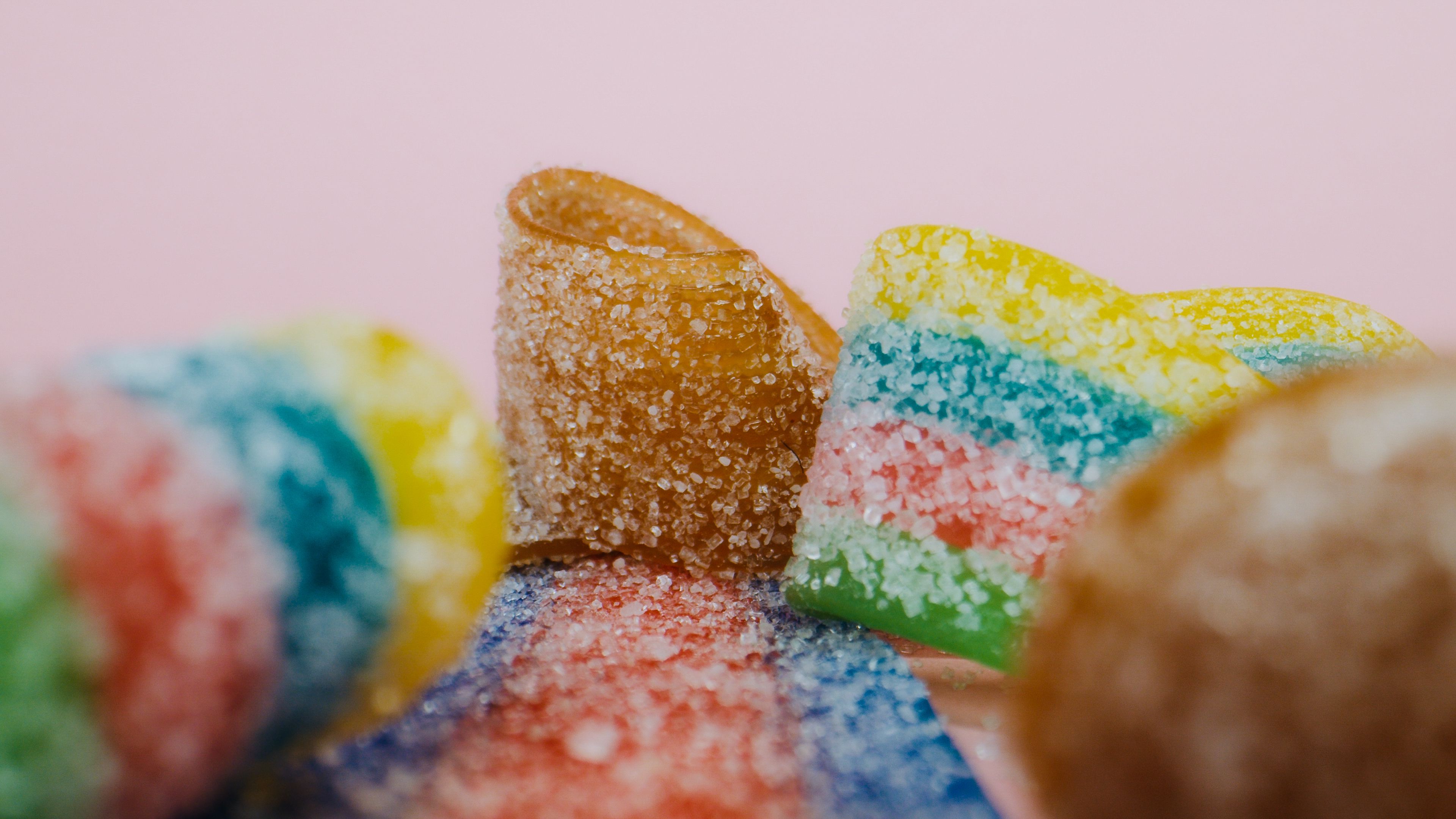 Vibrant close-up of multicoloured gummy candies with sugar coating on a pink backdrop.