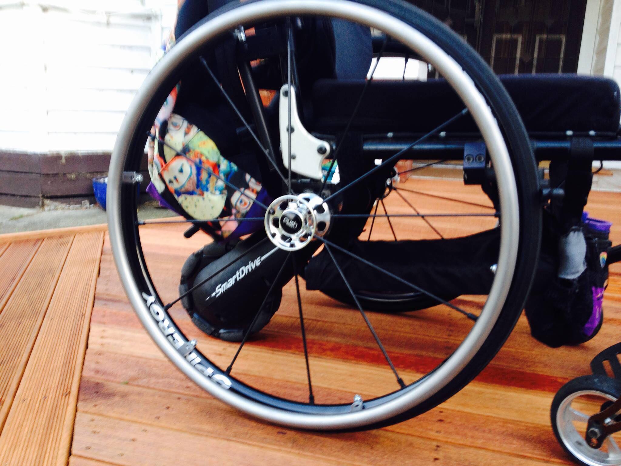 Image of a wheel of a wheelchair on a wooden floor, a owl printed bag can be seen hanging on the back
