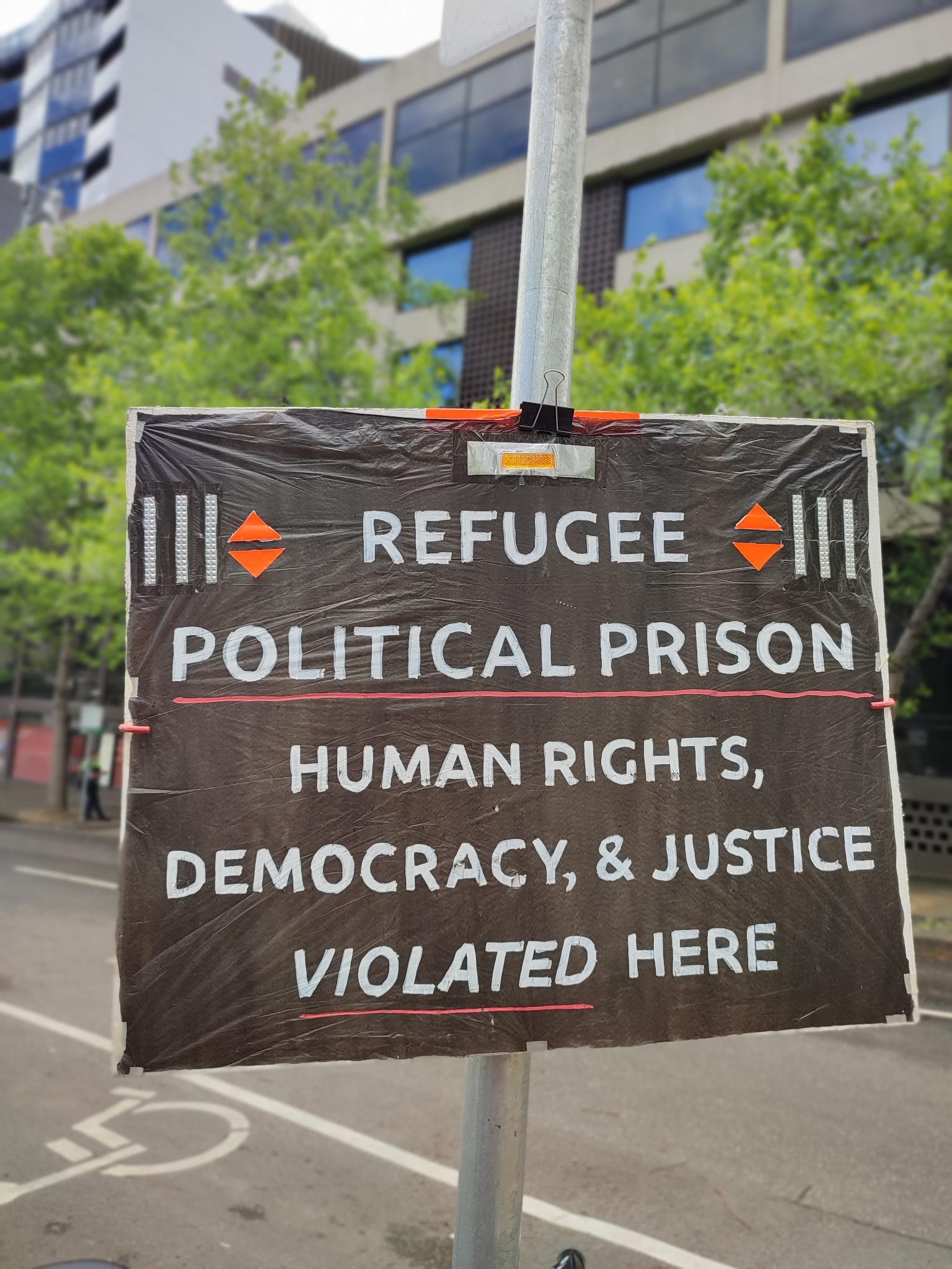 'Refugee Political Prison, Human Rights, Democracy & Justice Violated here' placard on a pole in front of refugee hotel prison in Melbourne.