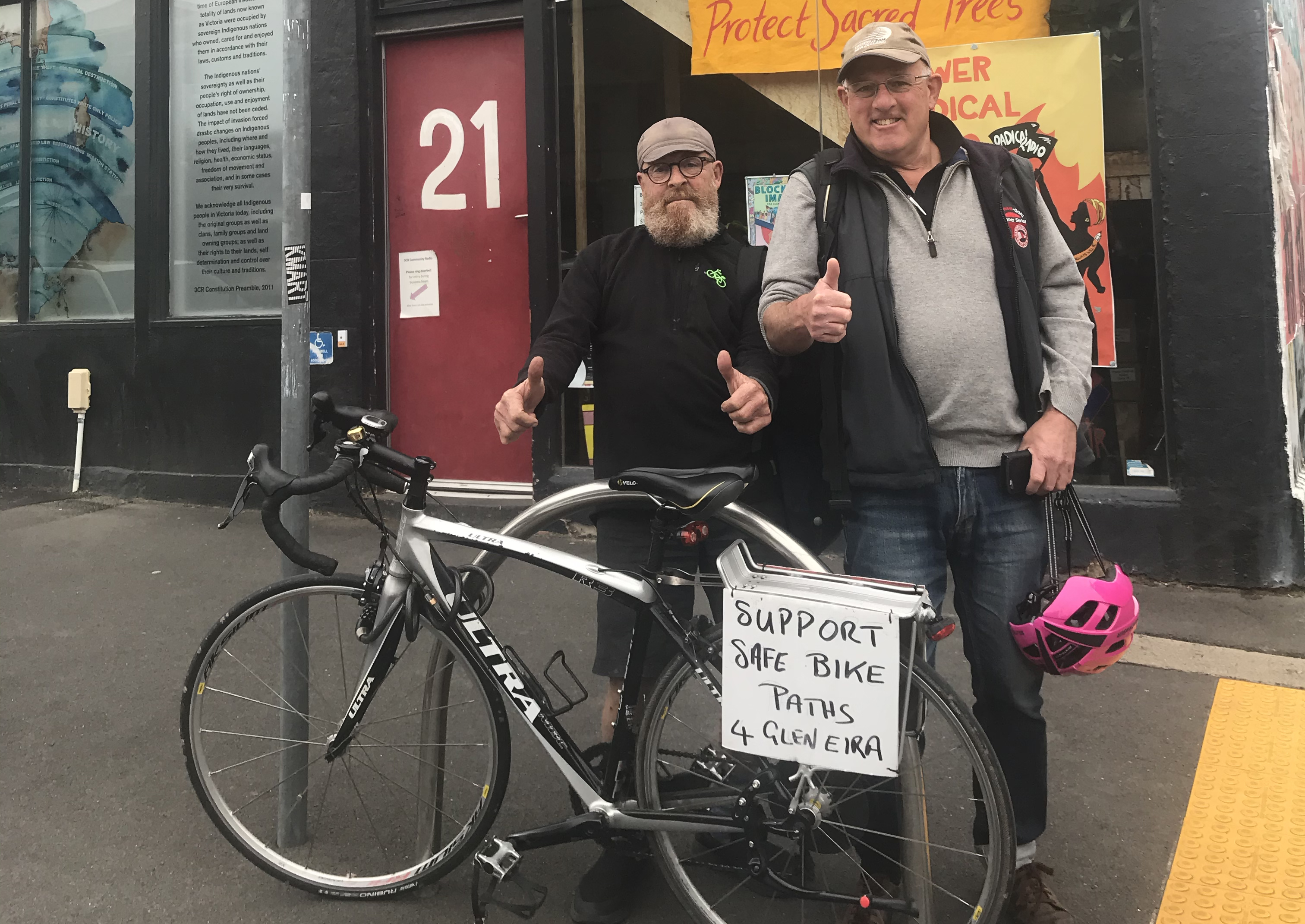 Val Nagle and Herschel Landes outside 3CR Community Radio with a sign supporting the safe cycling corridor in Glen Eira on Herschel's bicycle. 
