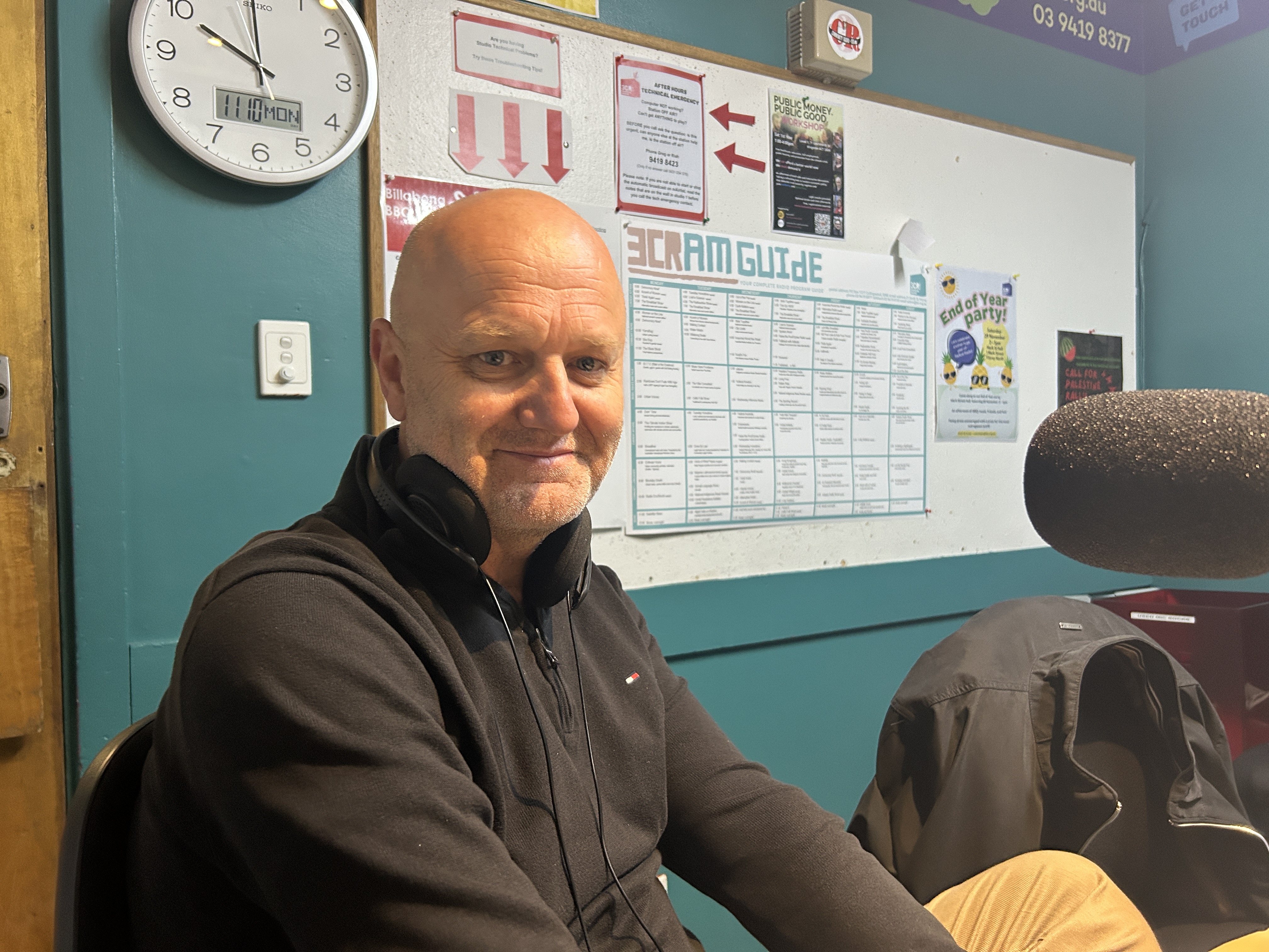 A man wearing a black top sits facing the camera and smiling