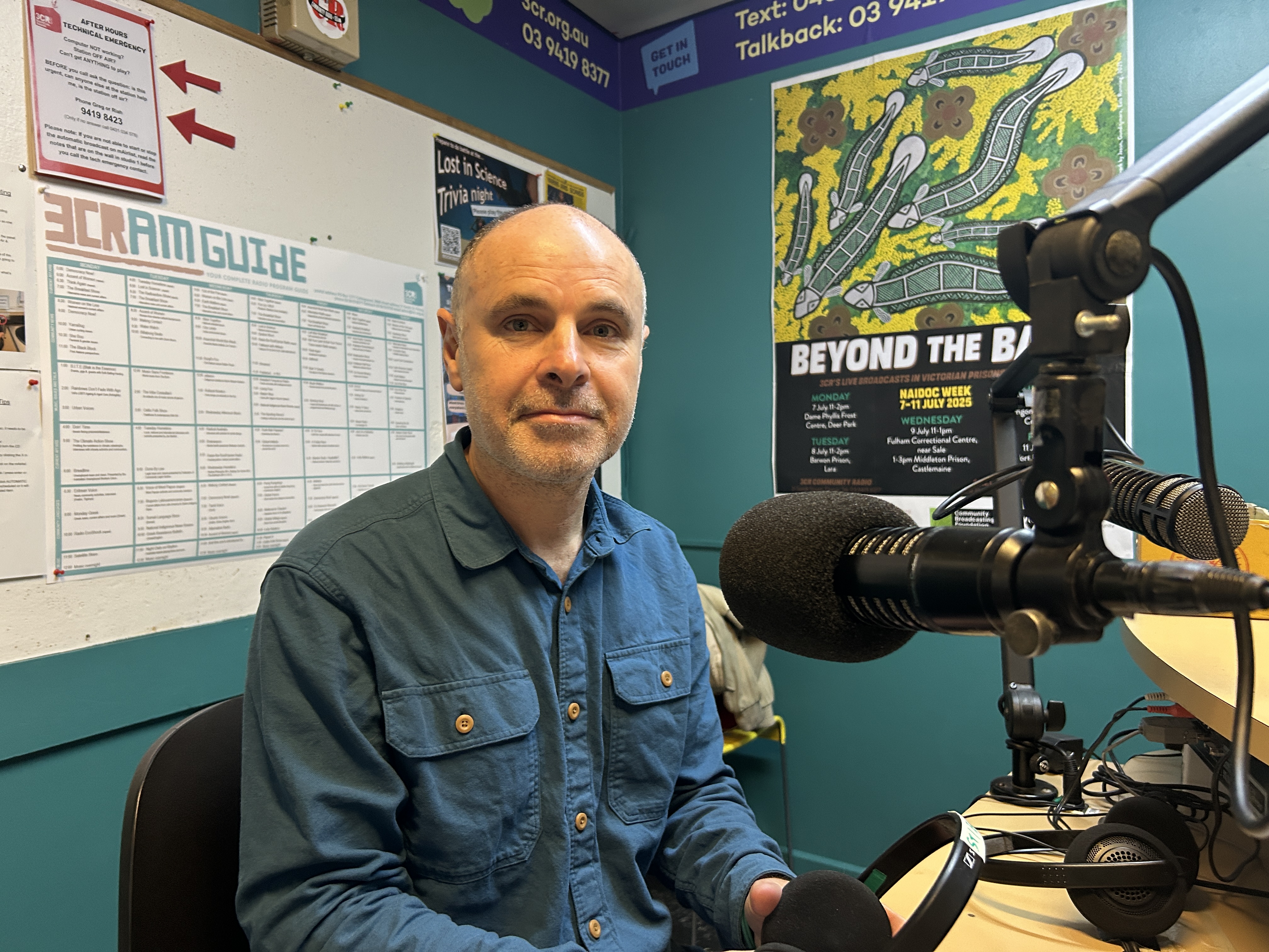 A man sitting in front of a microphone faces the camera 