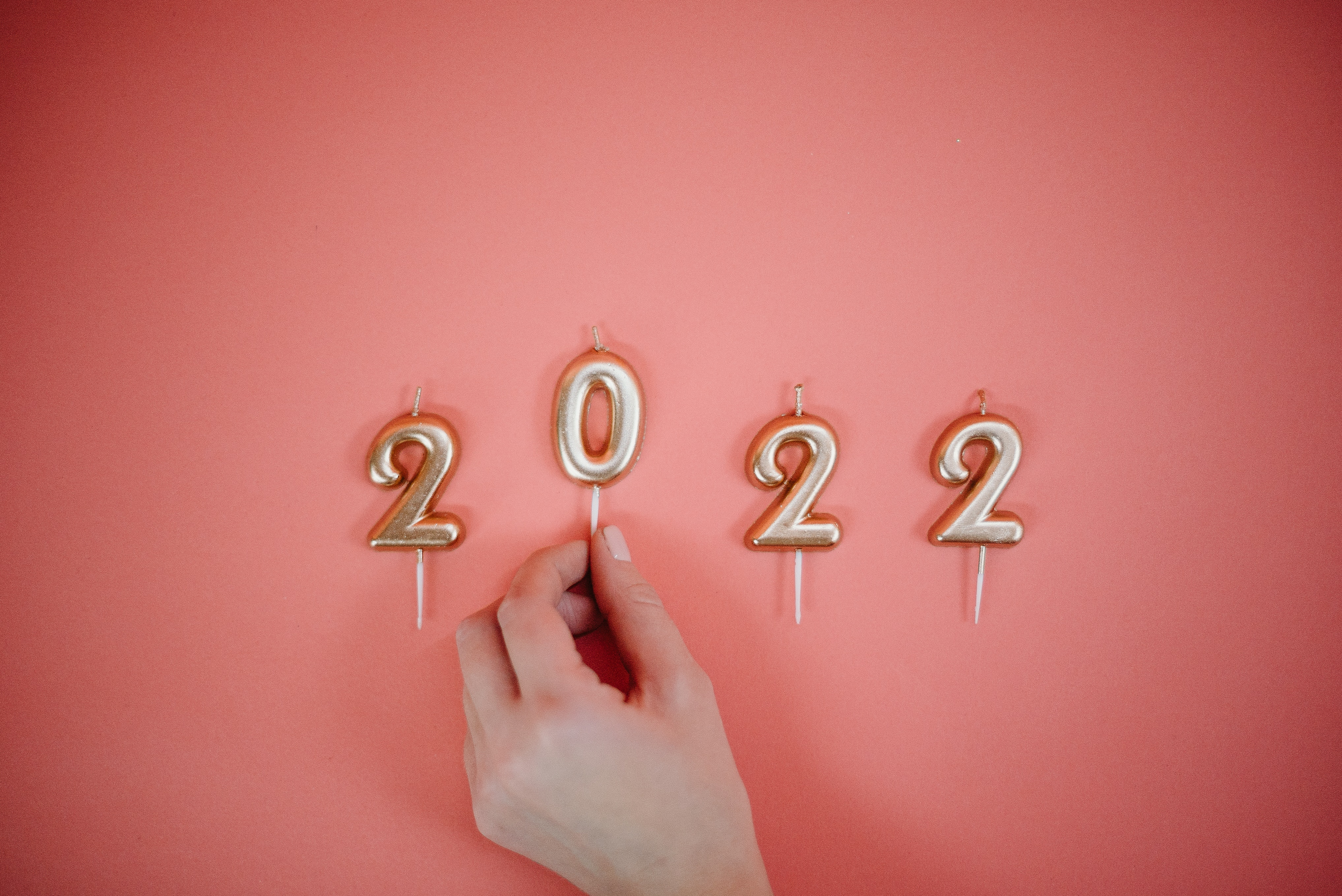 The numbers of 2022 laid out against a pink background as candles, with a hand that is moving the 0