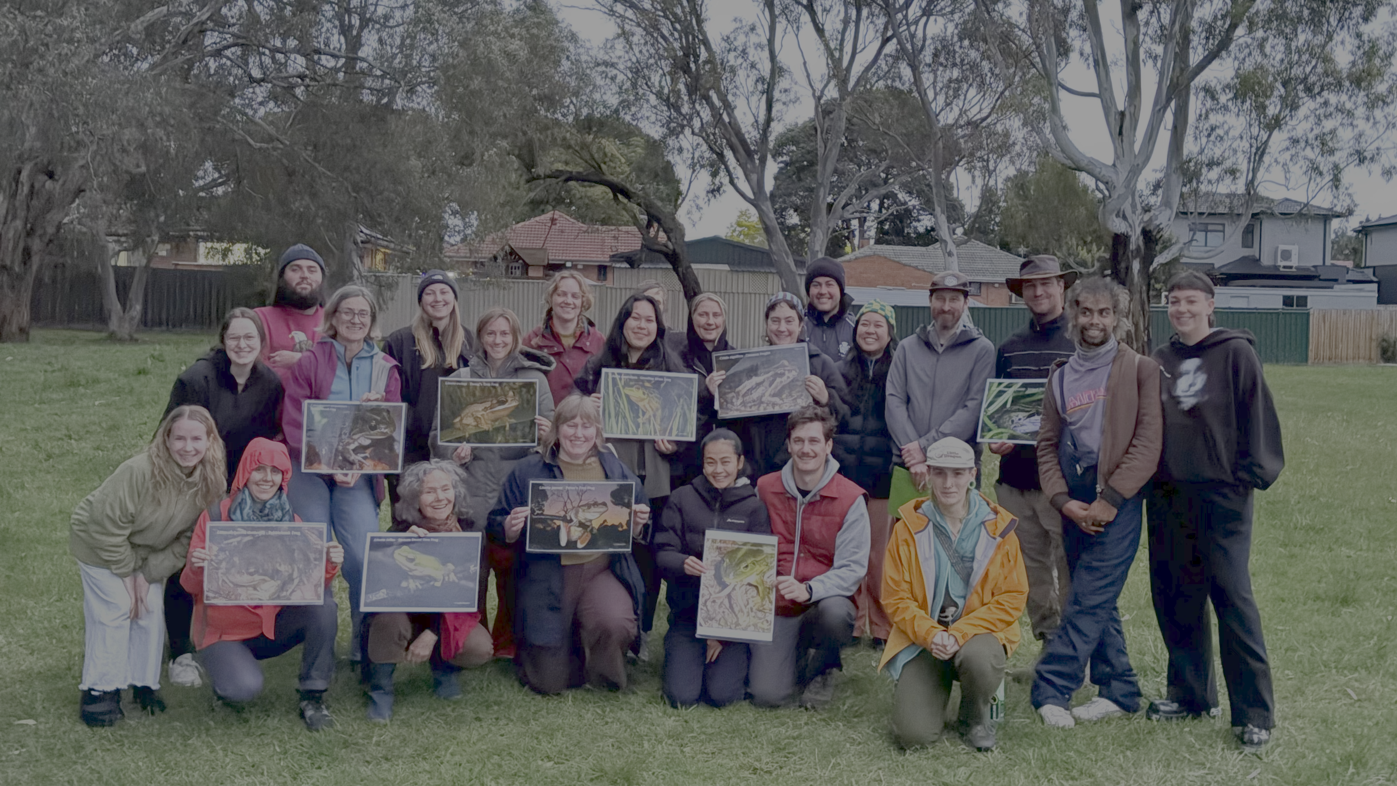 A photo of a group of DCMC's volunteers, smiling and showing images of frogs found at Darebin Creek. Provided by Darebin Creek Management Committee.