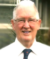 Bevan looks at the viewer. He is a white man with white hair and wears glasses.