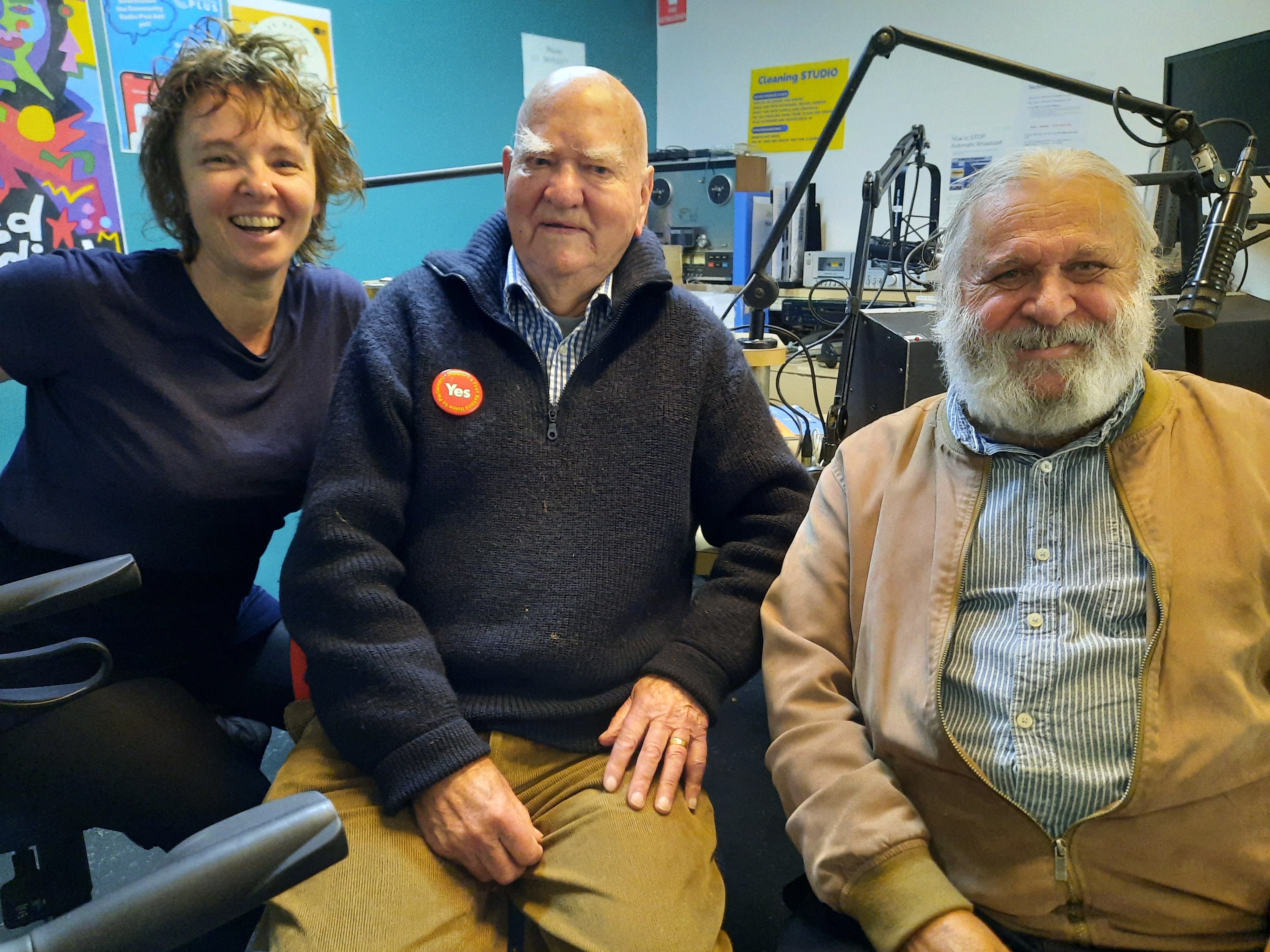 Kelly, Percy and Joe sit in a row in studio 1 at 3CR smiling at the viewer