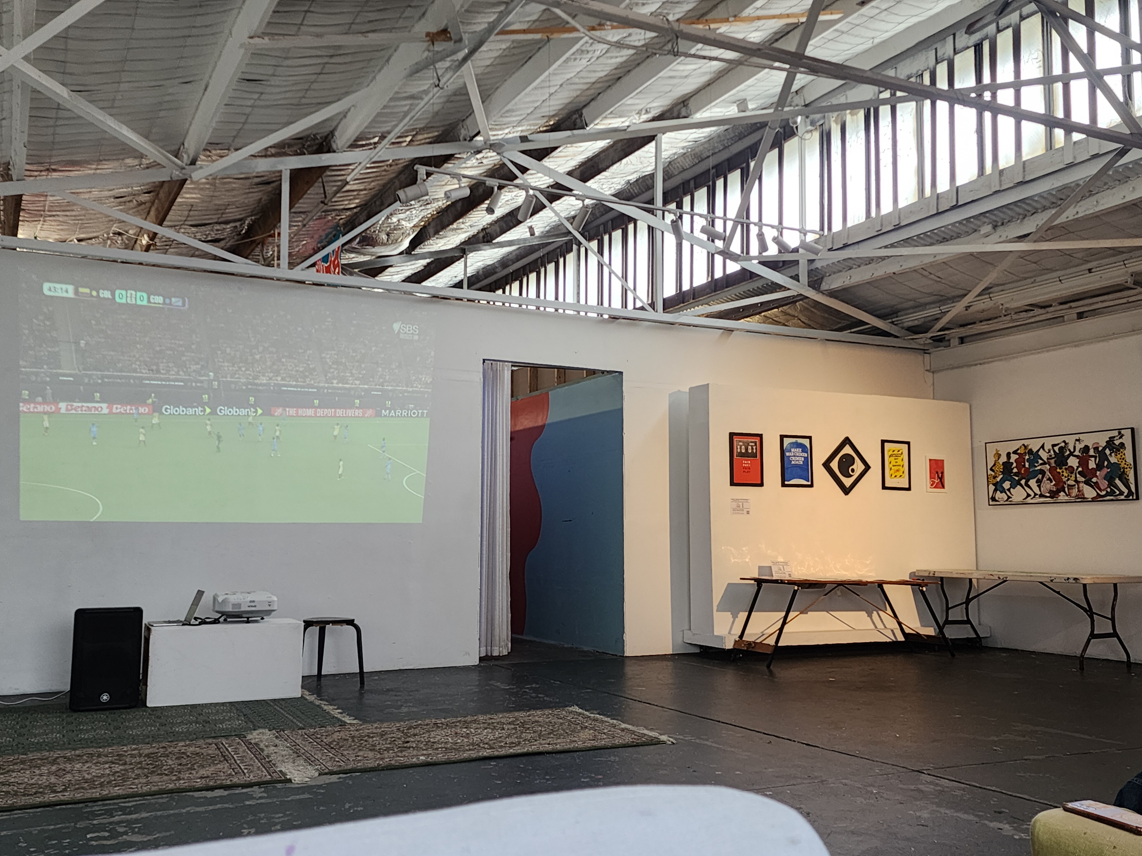 Image of world cup football game projected on wall of Lil Homey Cafe with artwork adjacent wall
