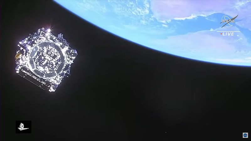 View from rocket of blue planet Earth in the upper right corner and silver telescope to the left, floating in dark outer space. 