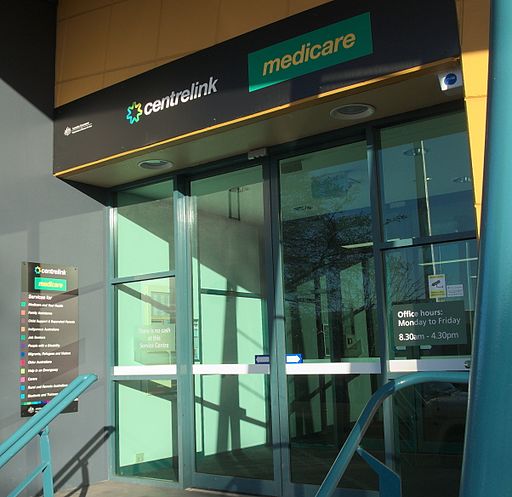 Glass sliding door entrance to a corporate building with text above door reading "CENTRELINK MEDICARE". 