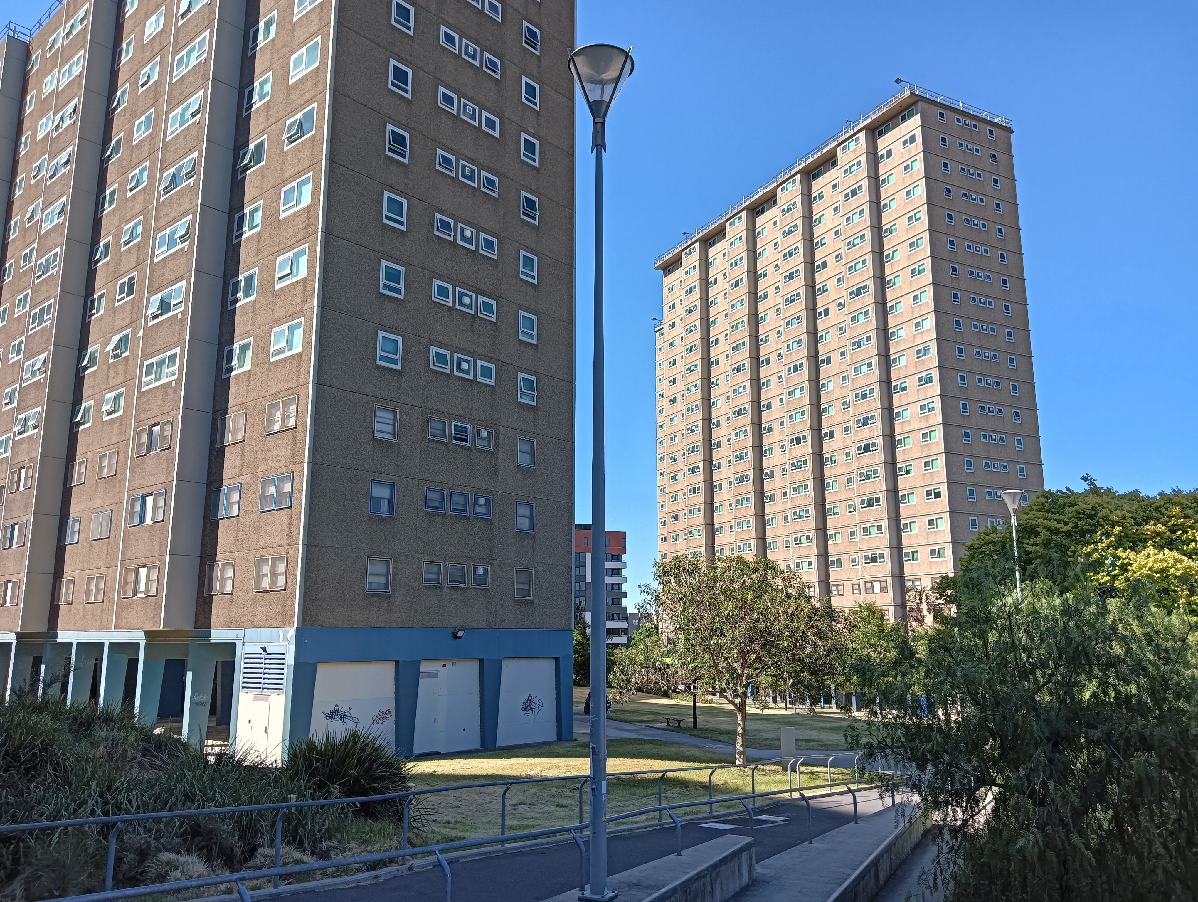 Public housing towers - one in partial view in the foreground, and one in full view in the background. It is a sunny day with a clear blue sky.