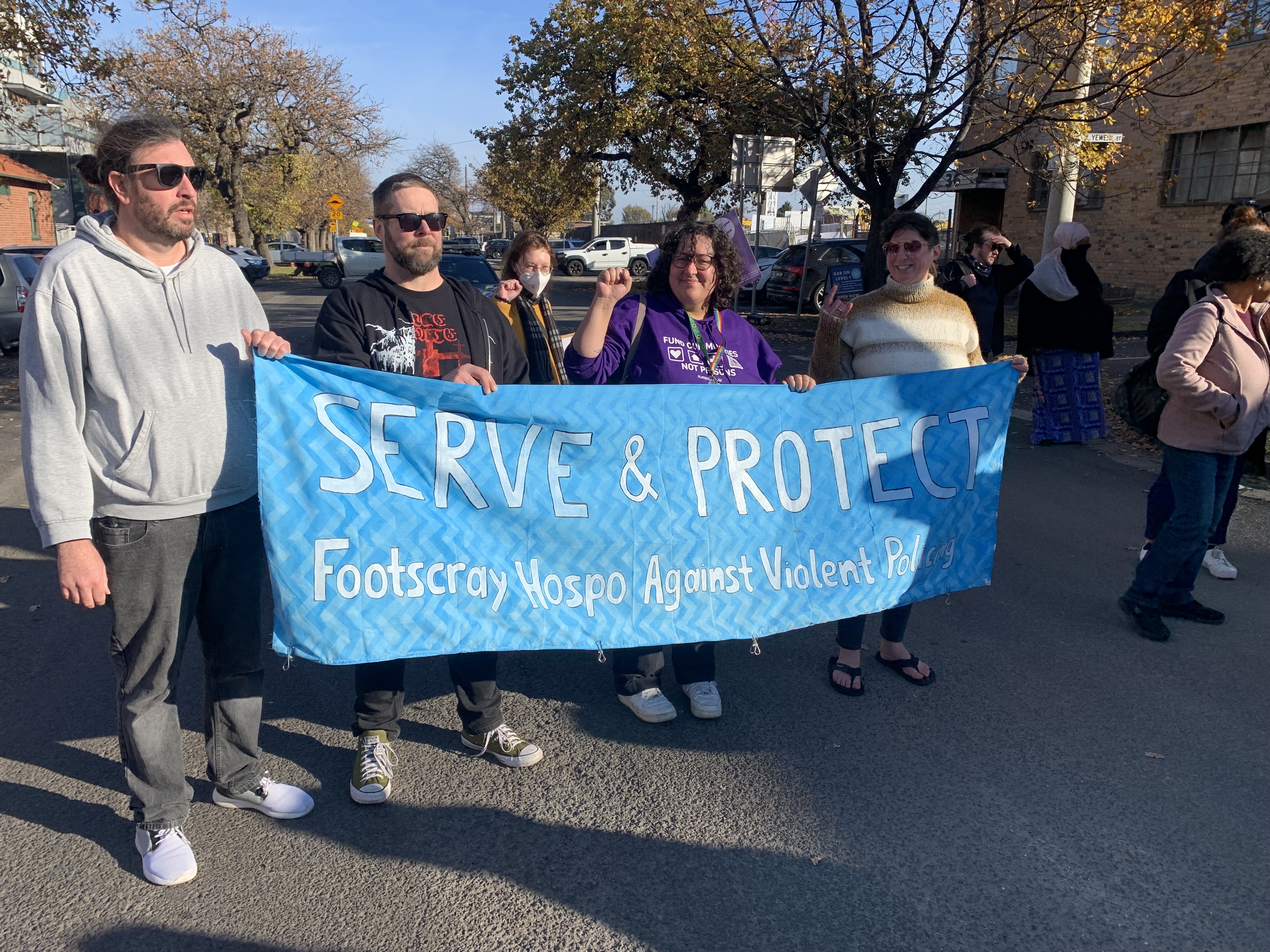 Footscray Hospo Workers Unite holding large blue banner with white font that reads ''Serve & Protect Footscray Hospo Against Violent Policing''