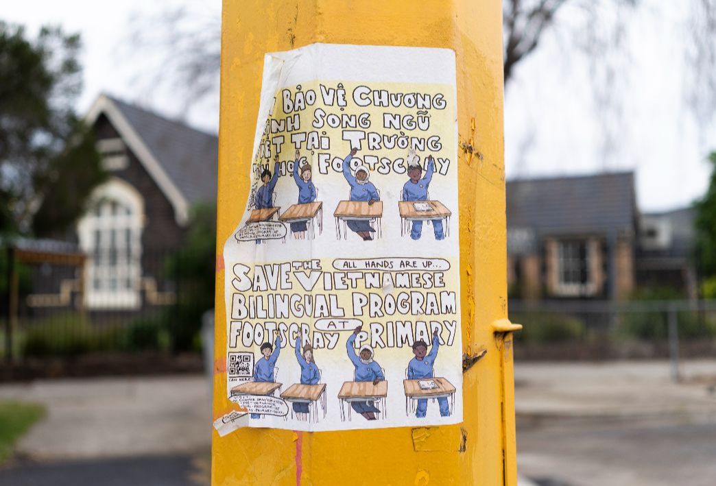 Paper campaign poster with an illustration of children at school desks reading "Save the Vietnamese bilingual program at Footscray Primary", ​in both English and Vietnamese, stuck on a yellow post with one corner peeling free.