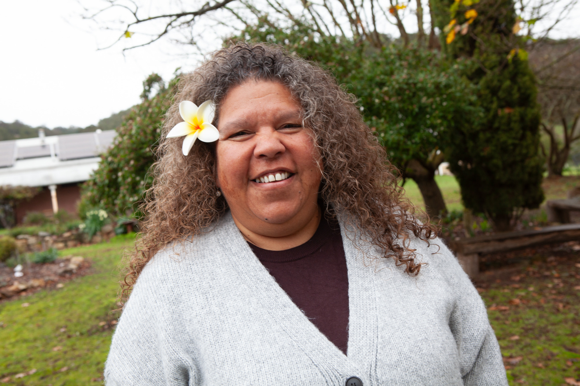 Image of Karina Lester, a Yankunytjatjara Anangu leader, second-generation survivor of British nuclear tests at Emu Field in South Australia, ICAN Ambassador, and Commissioner on the AUKUS Public Inquiry. She has a frangipani in her hair.