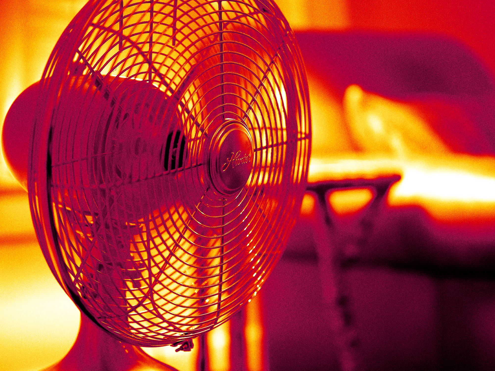 Electric fan in front of a bed, against red and orange background showing heat