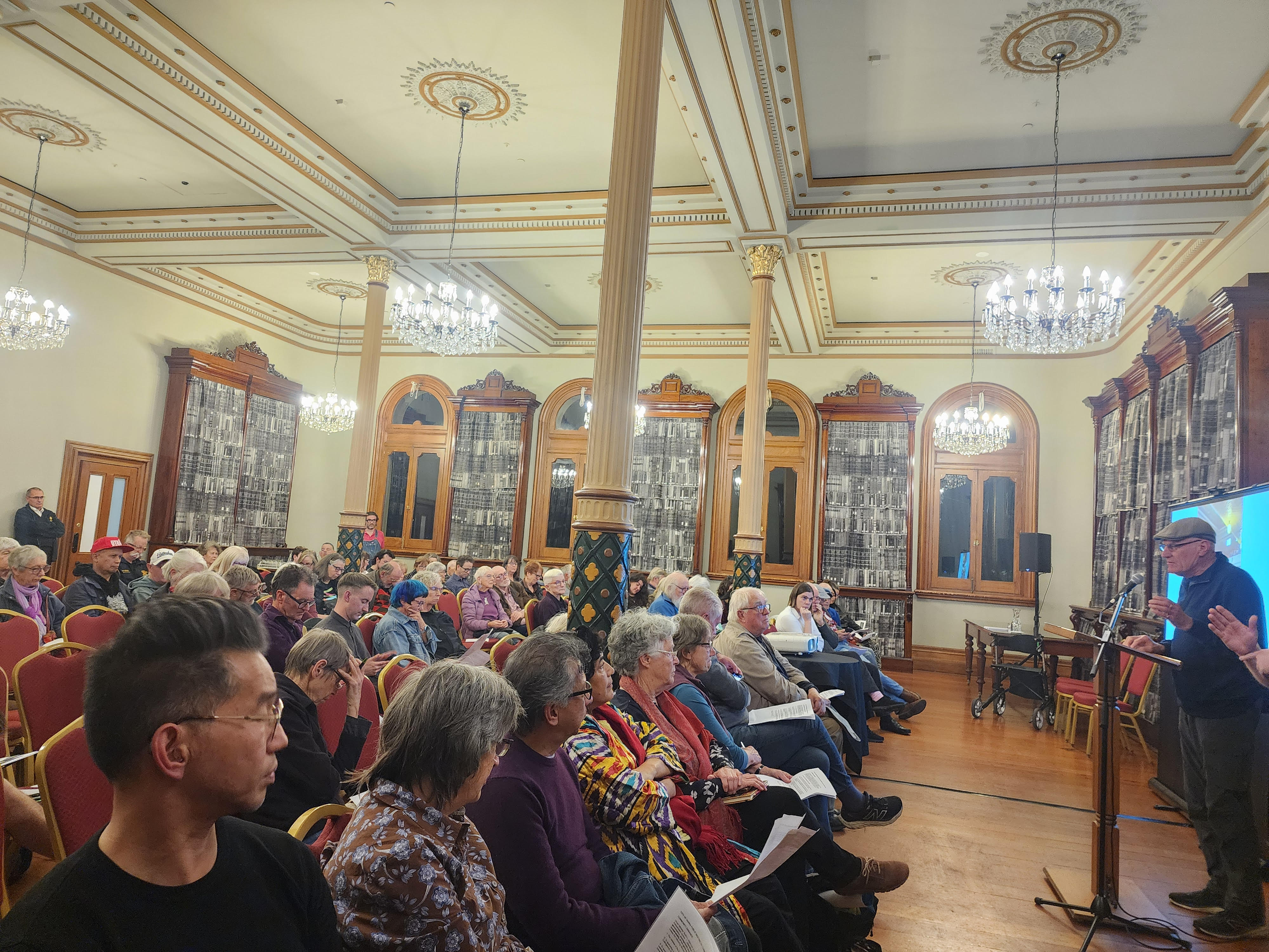 Town Hall meeting members sitting down looking at speaker at the front.
