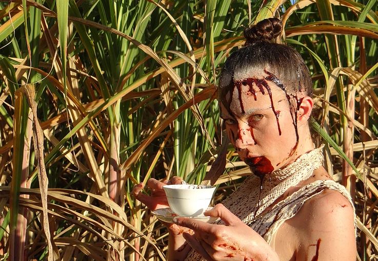 Lady Longdrop, performer, holding tea cup in front of a sugar cane field