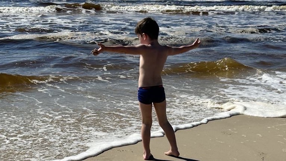 Young child standing with arms wide open towards the ocean