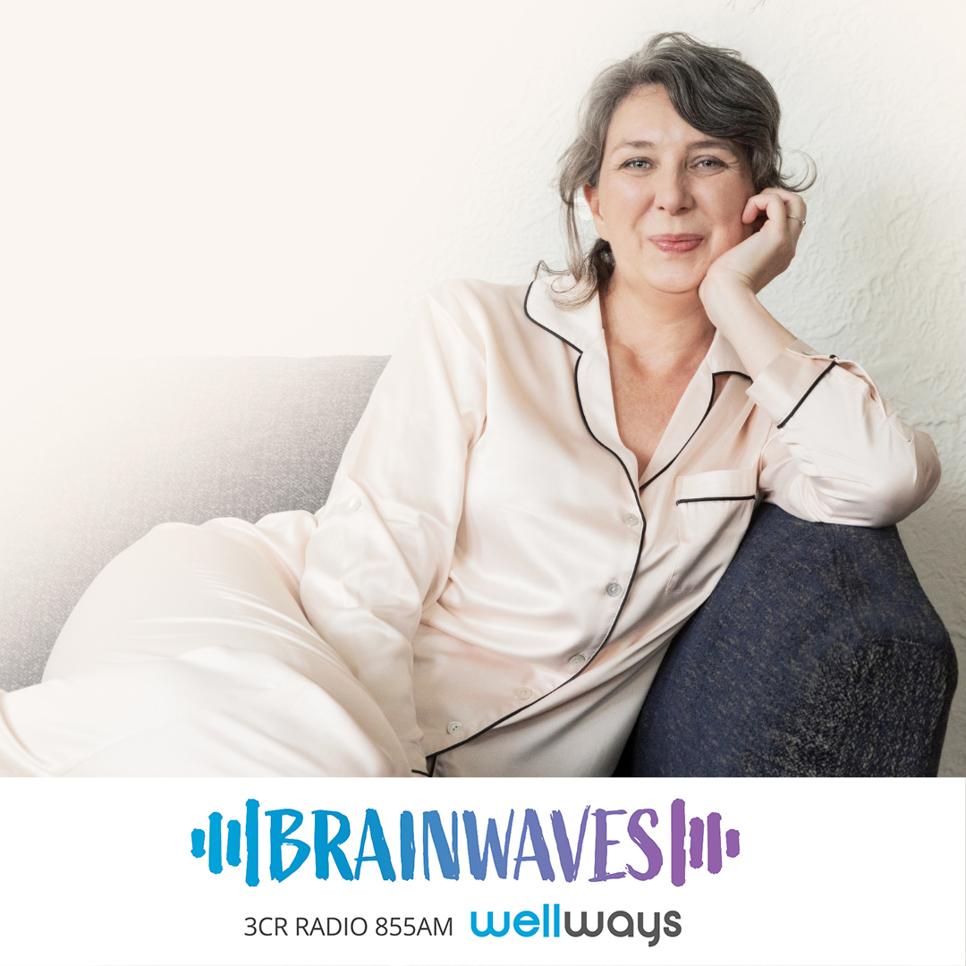 Michelle Irving is a caucasian woman with brown and grey hair pulled back, she is wearing cream pyjamas and is sitting on a couch smiling at the camera.