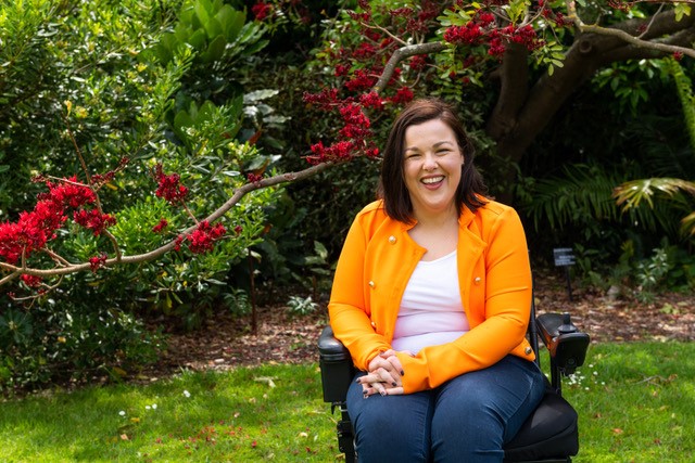 Peta Hooke has Cerebral Palsy and is sitting in a garden in her electric wheelchair.