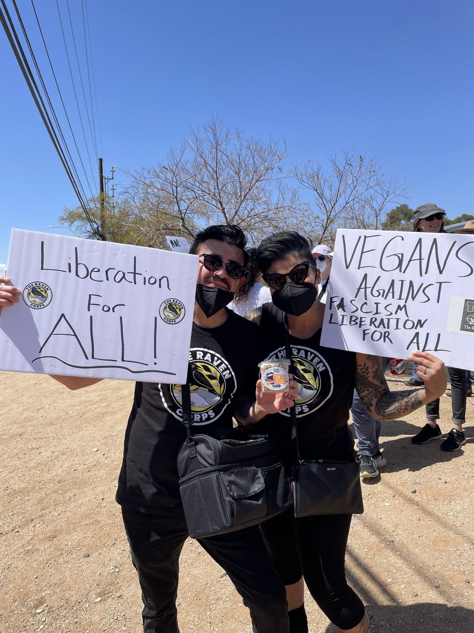 Photo of Claire and Jesse smiling and holding up signs saying Liberation for All and Vegans Against Fascism
