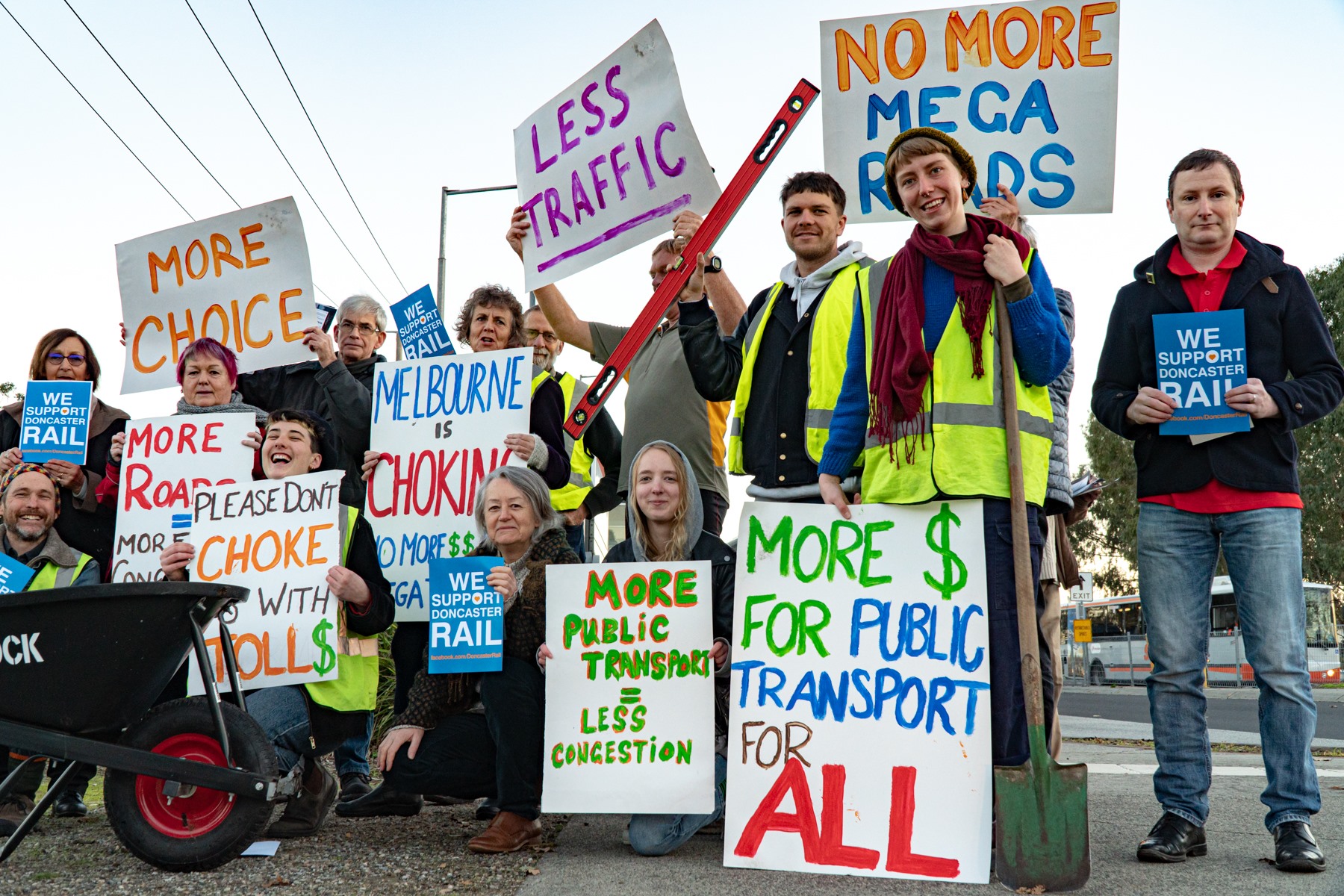 A group of activists of all ages holding signs opposing the construction of new roads and supporting public transport