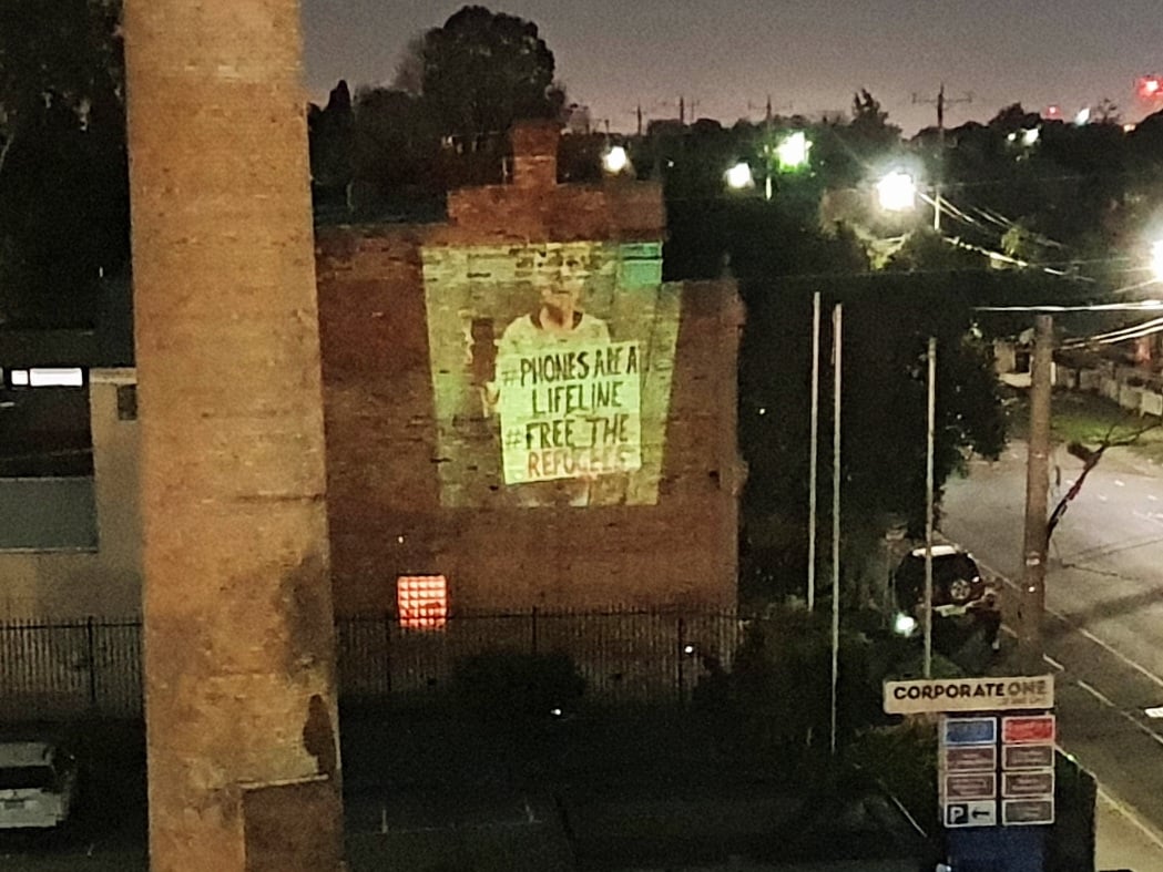 a projection on a  wall that said phones are a life line free the refugees 