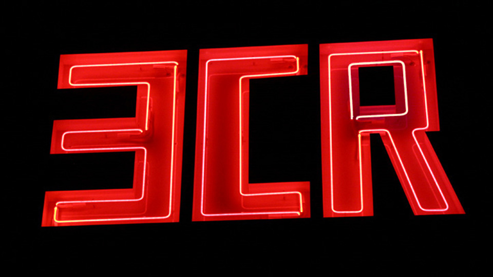 A close-up photograph of a bright neon sign which reads: 3CR