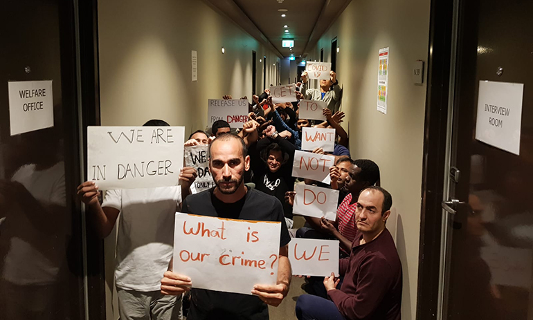 picture of Medevac refugees. inside  the hotel holding protest signs one said what is our crime