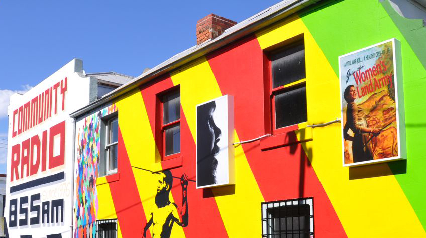 An image of the colourful mural on the side of the 3CR building, with painted words visible, reading COMMUNITY RADIO / 855AM