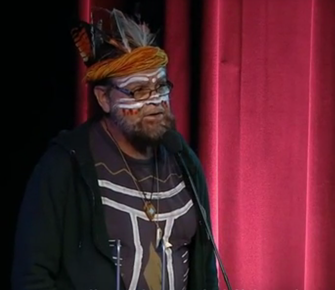 Uncle Bunna Lawrie in full face paint & t-shirt with body paint, and with ceremonial head dress & feathers at Equinor AGM