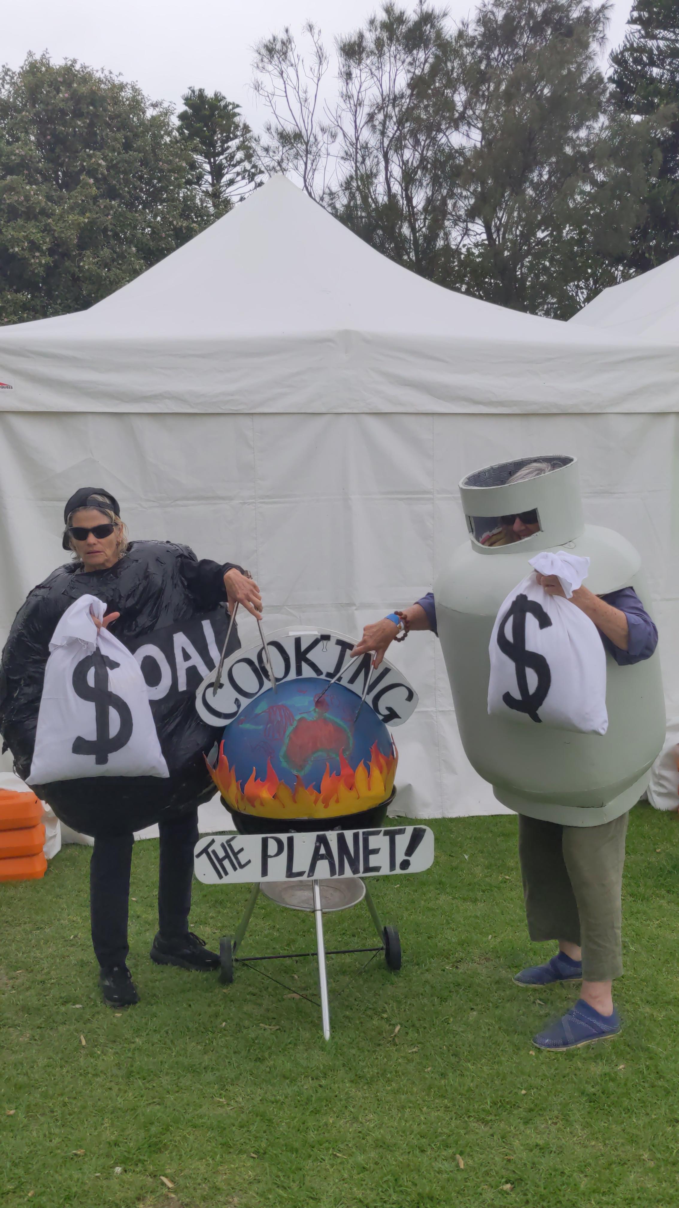 Two climate activists - one dressed as a lump of coal and one as a gas canister - cook an Earth on a BBQ with a sign that reads 'Cooking the planet!'