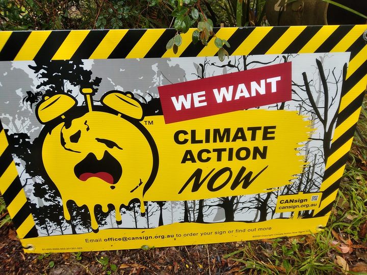 A yellow and black sign with a melting clock with alarmed face. Climate Action Now