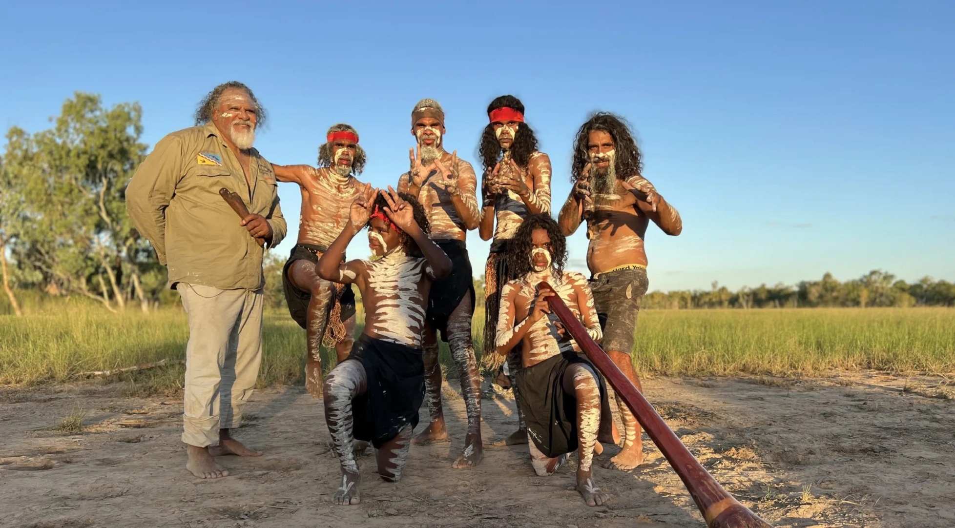 Five men painted in dance pose with digeridoo