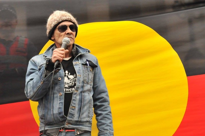 Djuran Bunjileenee Borun MunDunDarung, aka Robbie Thorpe. standing in front of Aboriginal flag giving a speech at an unspecified rally