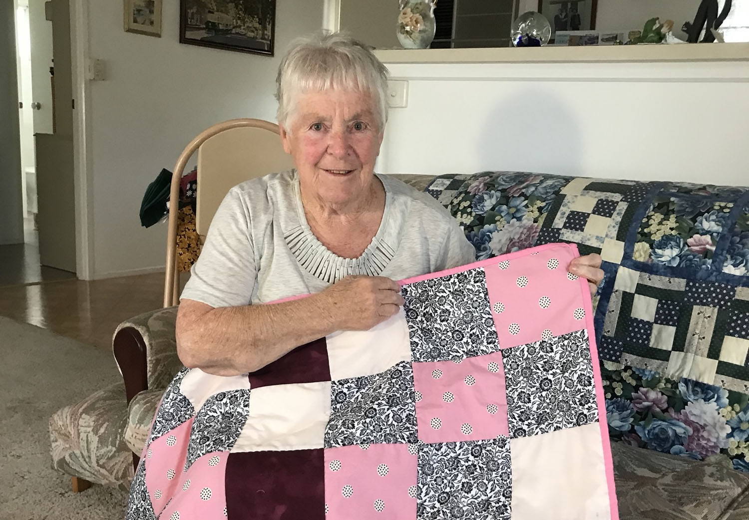 An older white women holds up a handmade quilt
