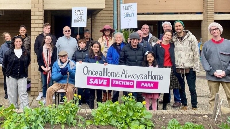 A group of residents standing outside a house with a banner reading Once A Home, Always A Home: Save Techno Park