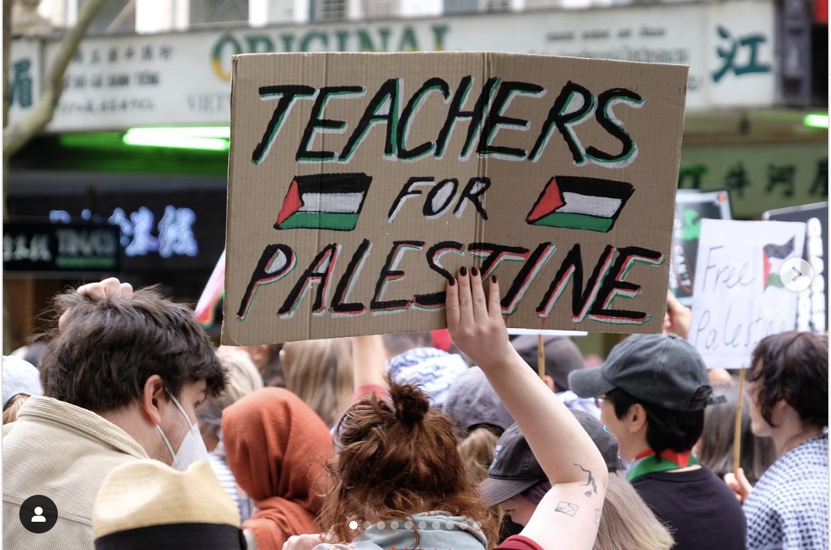 A person holding up a cupboard placard in a crowd that reads Teachers for Palestine