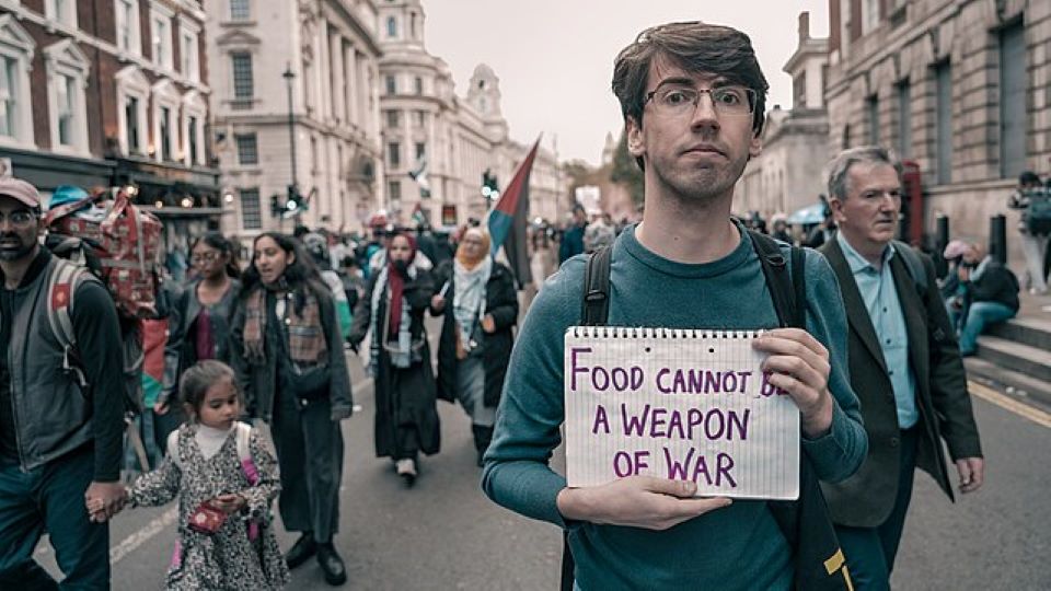 A man holding a sign which is written on it "Food cannot be a weapon of war"