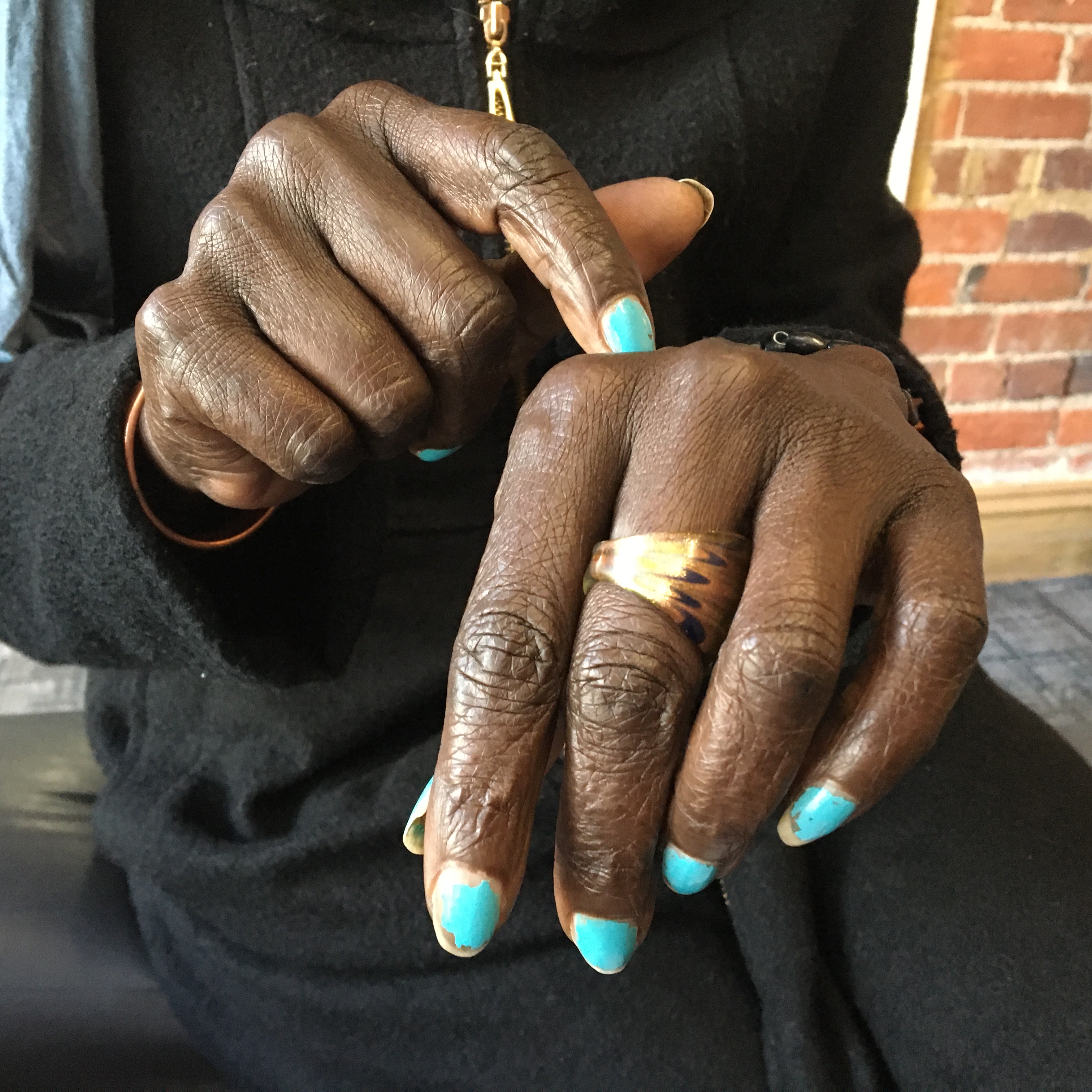 Two brown skin hands with aqua painted nails, one finger points to the top of the other hand.