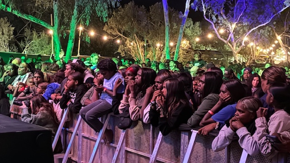 A crowd of people gathered at the foot of a rock concert stage in the outdoors at night