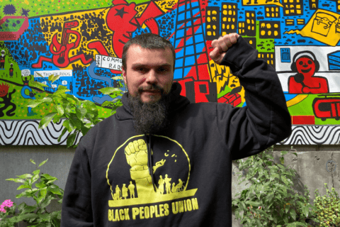 Keiran Stewart-Assheton in the 3CR garden wearing a Black Peoples Union hoodie and holding up a raised fist