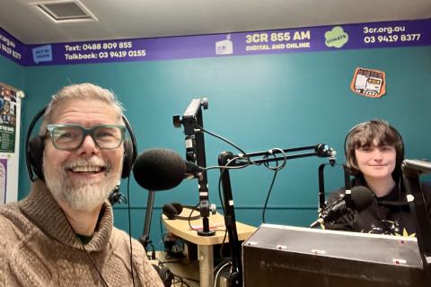 Amy and Keir sitting in the 3CR studio with their headphones on smiling for a sefie.