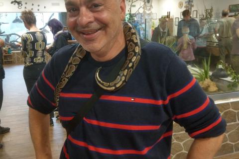 John Tzimas blue shirt horizontal red stripes short white hair snake around neck.