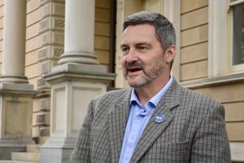 Rodney Croome short salt and pepper coloured hair checked jacket light blue shirt open at neck old official building in background