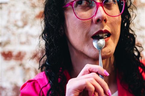 Woman dark hair pink glasses pink jacket teaspoon to mouth