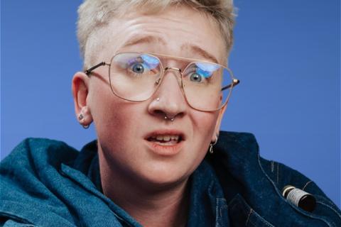 Eddie Patterson short blonde hair, large rimless glasses aqua coloured top